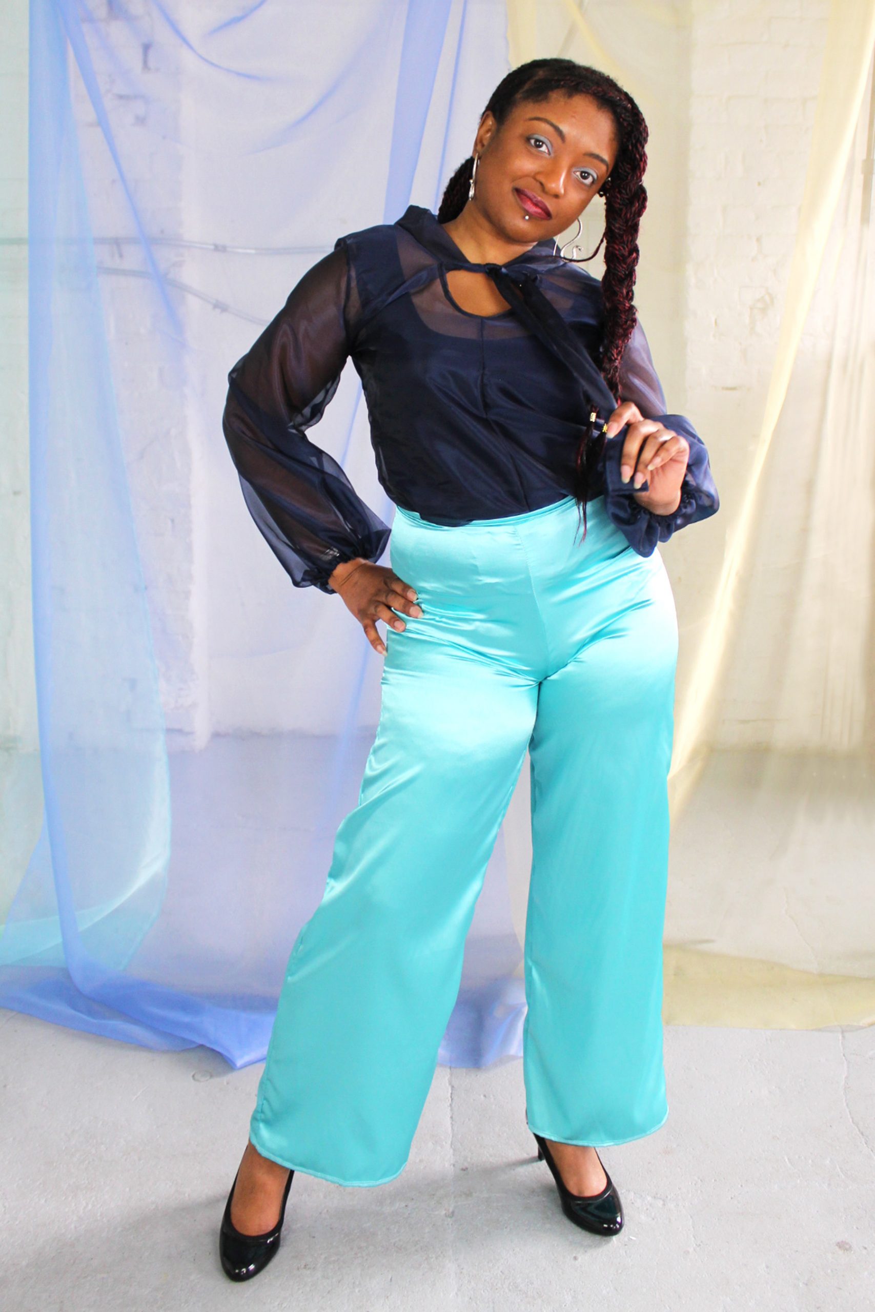 Straight size black model with braided hair wearing navy organza blouse with neck tie + bell sleeves with seafoam satin pants