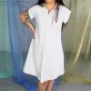 Smirking straight size white female model with one arm modeling white multi color polka dot button front collared shirt dress