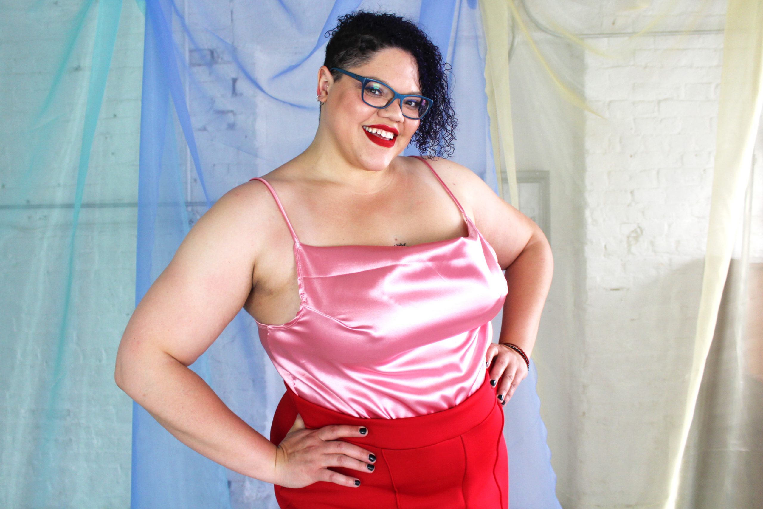 Confident plus size tall black model with curly short hair wearing red suit and pink satin camisole, ethically made in NYC