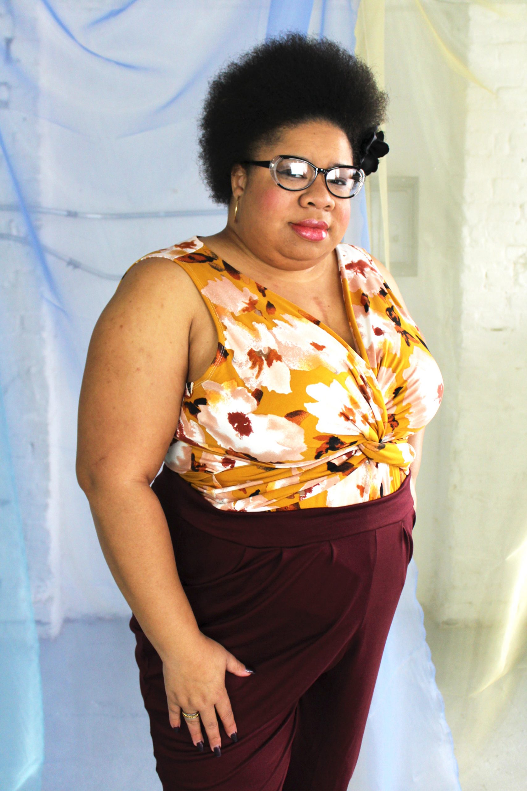 Plus size black model with afro and glasses modeling jersey tank with twist detail in mustard and wine color floral print