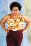 Plus size black model with afro and glasses modeling jersey tank with twist detail in mustard and wine color floral print