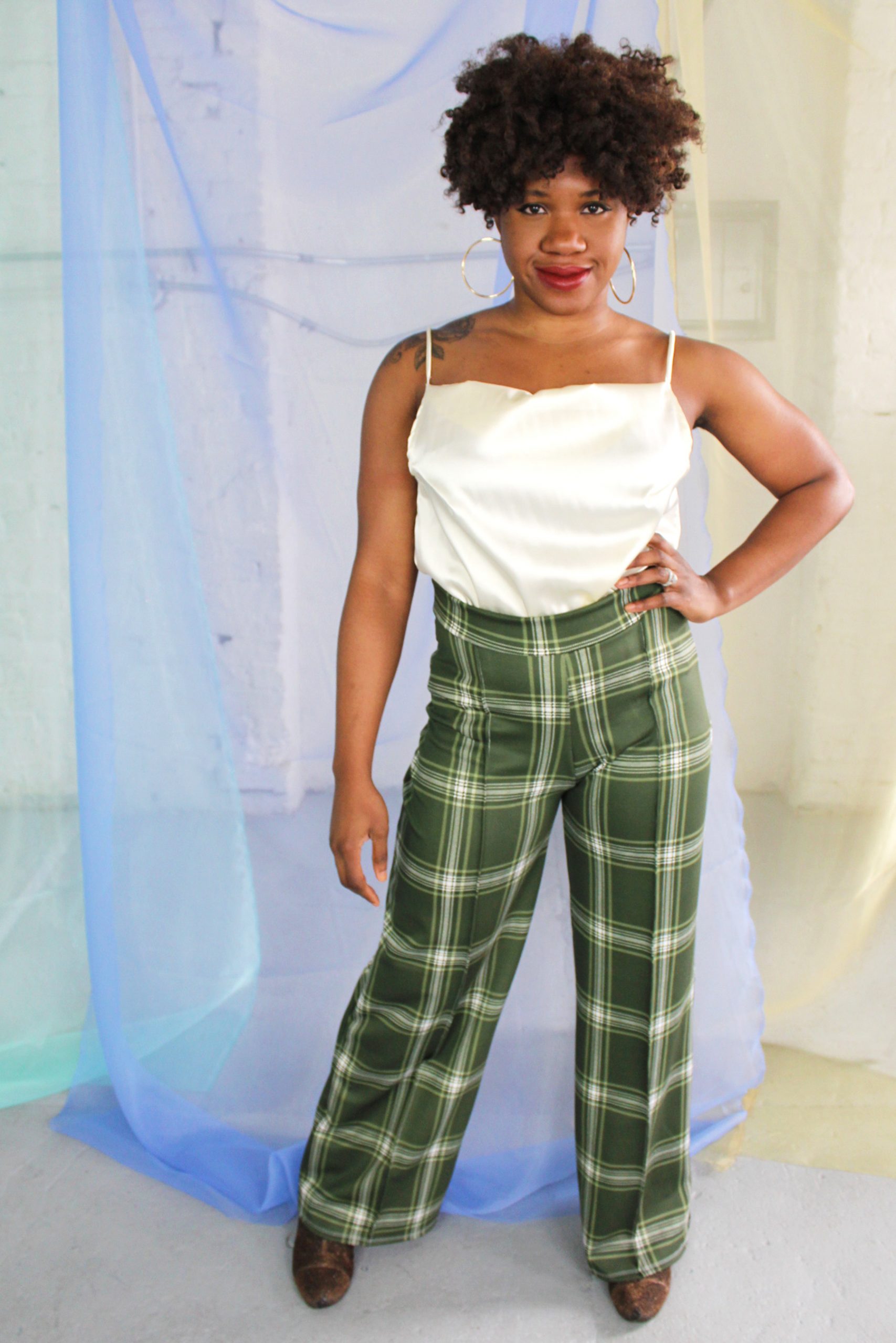 Confident straight size black model with curly short hair wearing green plaid suit and cream satin camisole, handmade in NYC