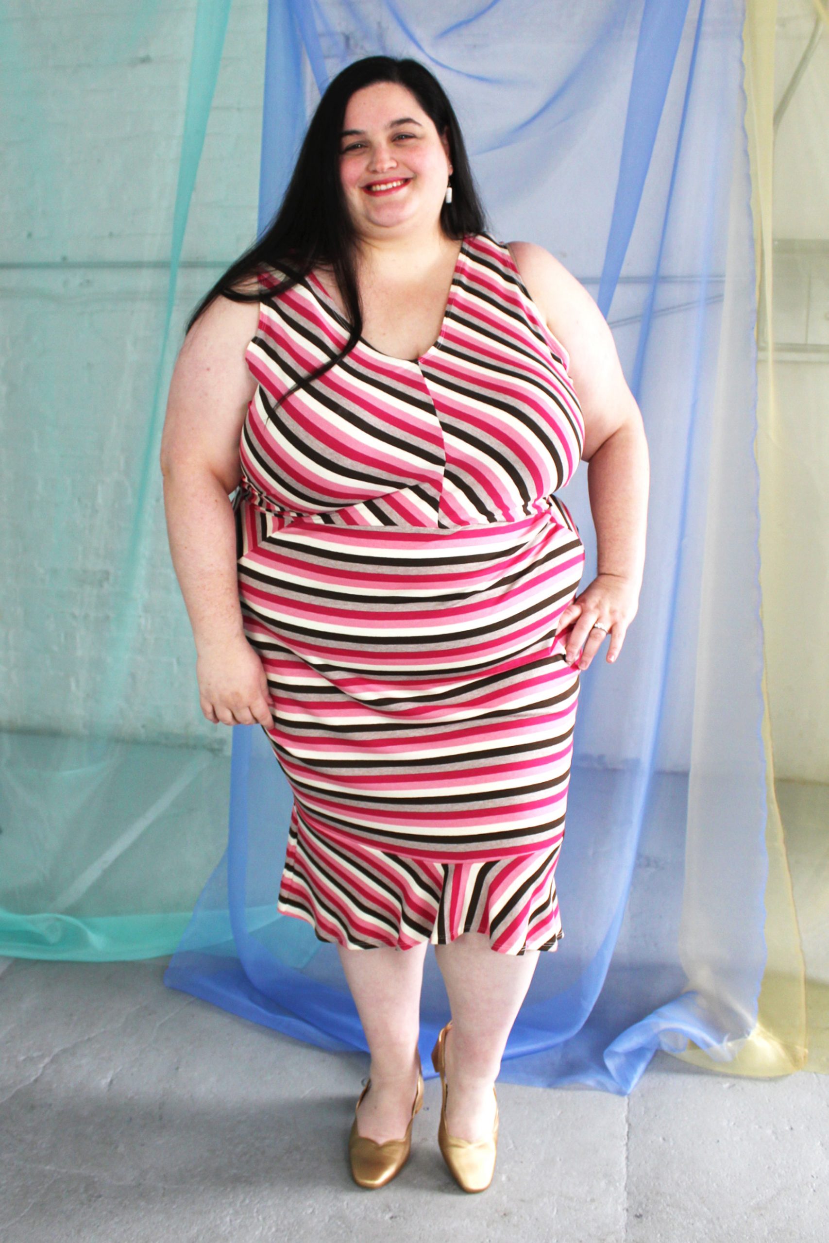 Pink and tan v-neck striped dress with pencil skirt and ruffle hemline modeled by plus size white model with long brown hair.