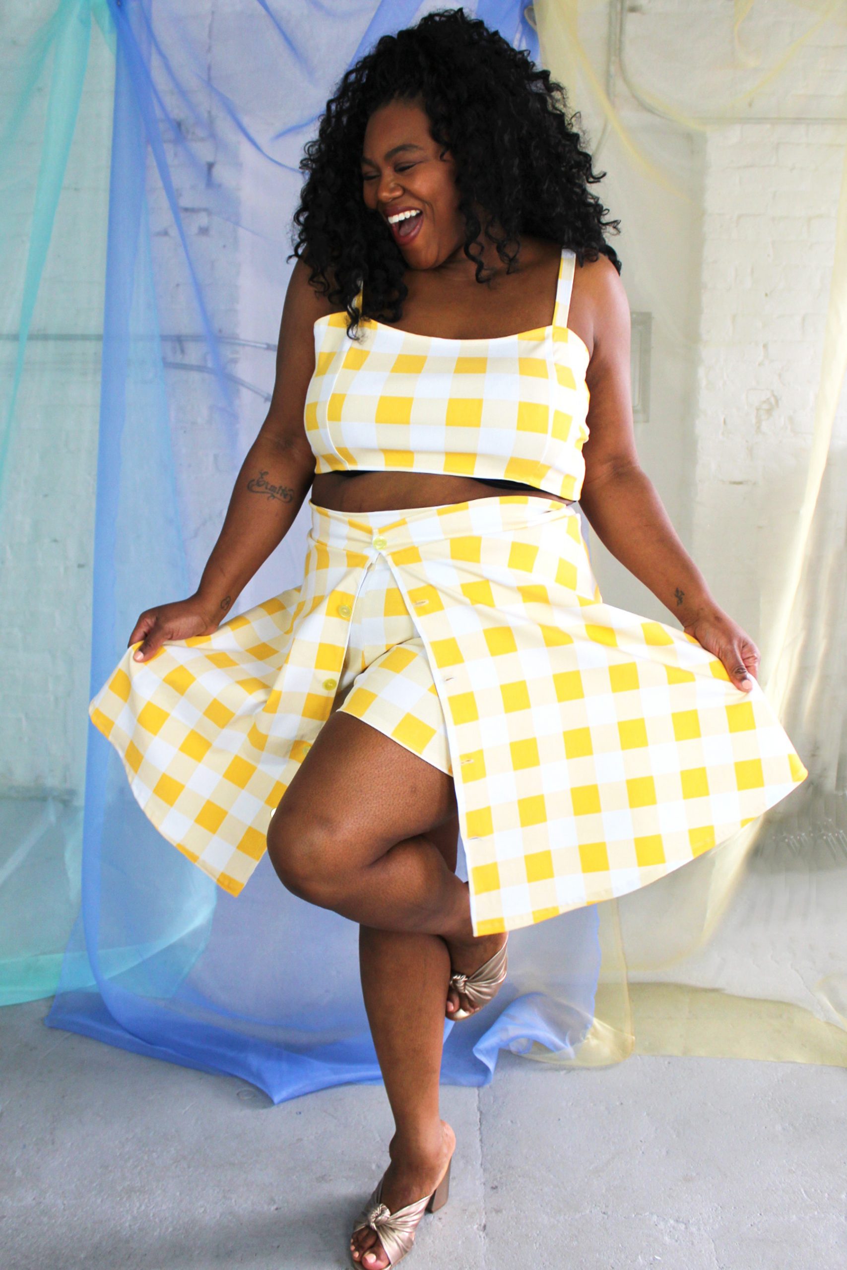 Black smiling plus size model modeling yellow and white check crop top, shorts, and over skirt - ethically handmade in NYC